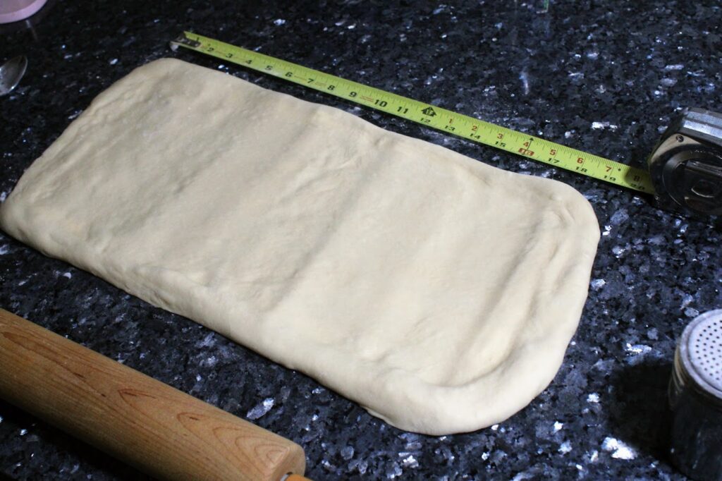 Dough that has been rolled into a 10 x 20-inch rectangle. There is a tape measure visible along the 20-inch side.